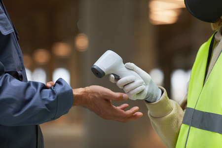Side view close up of supervisor measuring temperature of workers with contactless thermometer pointing at hands, copy spaceの写真素材
