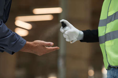 Side view close up of supervisor sanitizing hands of workers with spray , corona virus safetyの写真素材