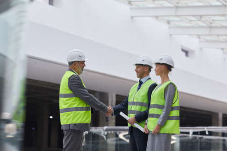 Side view portrait of smiling business people shaking hands after investment deal at construction site, copy spaceの写真素材