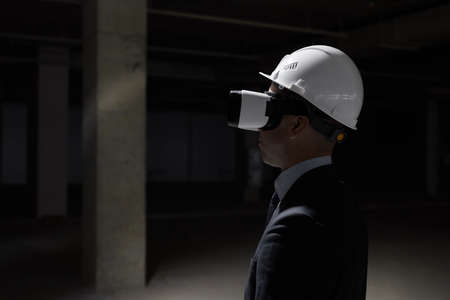 Dark side view portrait of businessman wearing VR gear at construction site while visualizing future project in 3D, copy spaceの写真素材