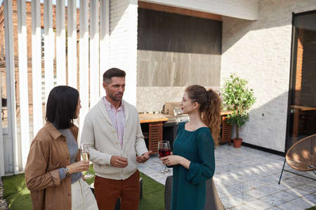 Waist up portrait of contemporary adult people chatting while standing at outdoor terrace during party, copy spaceの写真素材