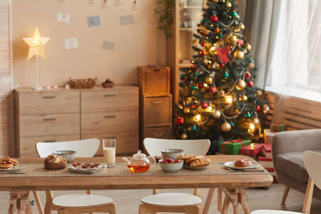 Background image of cozy home interior with Christmas tree and wooden table with snacks in foreground, copy spaceの写真素材