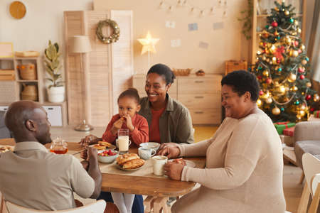 High angle portrait of happy African-American family enjoying tea and snacks while celebrating Christmas at homeの写真素材