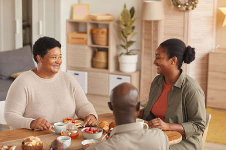 Warm toned portrait of African-American family enjoying tea and snacks while eating breakfast at...