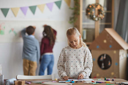 Portrait of smiling blonde girl standing by crafting table and enjoying art class in school, copy spaceの写真素材