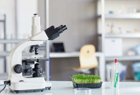Background image of electronic microscope and plant saplings on equipment table in biotechnology...