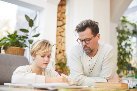 Portrait of modern mature father doing homework with teenage boy at home, parenting concept, copy...