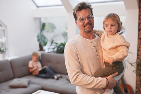 Waist up portrait of happy mature father holding cute little girl and looking at camera while standing in modern home interior, copy spaceの写真素材