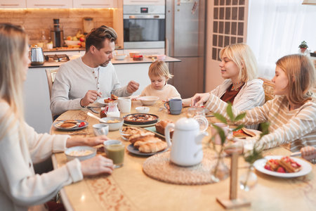 Wide angle portrait of big happy family enjoying breakfast together in kitchen , focus on father helping cute baby girl, copy spaceの写真素材