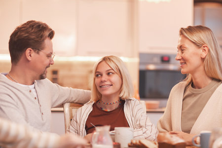 Portrait of mother and father looking at smiling teenage girl while enjoying breakfast together in...