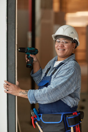 Vertical portrait of modern female worker smiling at camera while building wall on construction siteの写真素材