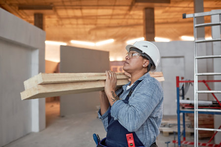 Waist up portrait of modern female worker carrying wood boards while working on construction site,...