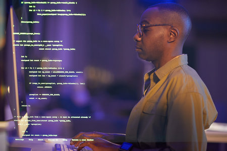 Side view shot portrait of modern African American man wearing eyeglasses working on computer code late in eveningの写真素材