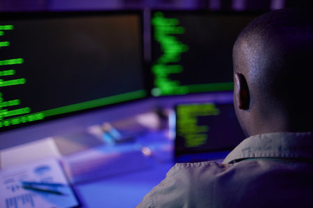 Unrecognizable African American soft developer sitting at desk in front of computers working on new code, rear view shotの写真素材