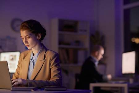 Modern office managers sitting at desks in dark room focused on their work using computers, copy...