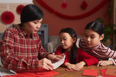 Beautiful Asian woman wearing red checked shirt spending time with her daughters at home making paper cranesの写真素材