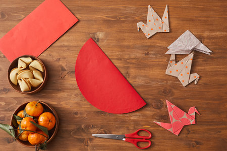 Conceptual top-down flat lay shot of tangerines, fortune cookies, paper cranes, red envelope and colored paper on wooden table prepared for Chinese New Year celebrationの写真素材