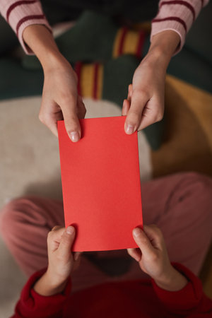 Vertical from above close-up shot of unrecognizable girls exchanging red envelopes on Chinese New...