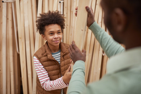 High angle portrait of smiling African-American boy shopping with father in hardware store helping in choosing wooden boards for construction or home improvementの写真素材