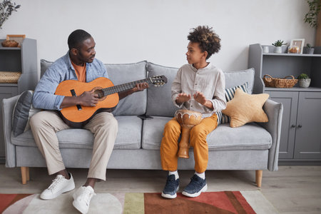 Horizontal full shot of African American man and his son spending time together at home playing guitar and djembeの写真素材