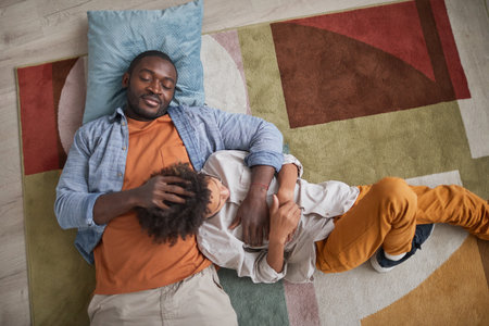 From above view shot of loving African American father relaxing on floor at home with his young sonの写真素材