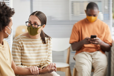 Portrait of caring mother comforting son while waiting in line at medical clinic or hospital, both wearing masks, copy spaceの写真素材