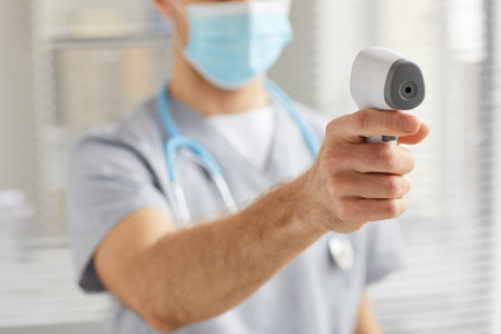 Close up of unrecognizable male doctor pointing infrared thermometer at camera while checking temperature in clinic, copy spaceの写真素材