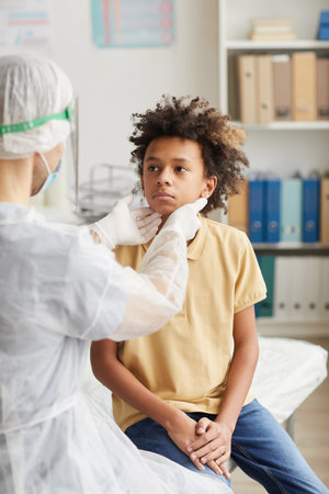 Vertical back view portrait of doctor examining African-American boy during consultation in covid clinicの写真素材