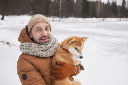 Waist up portrait of smiling mature man holding dog and looking at camera while enjoying walk in winter forest, copy spaceの写真素材