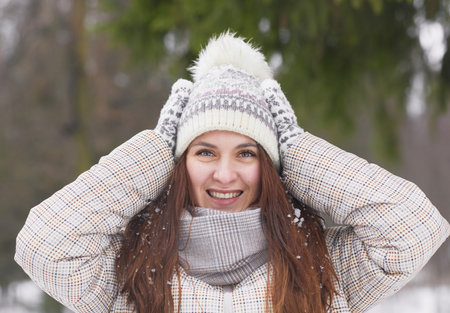 Front view portrait of happy young woman in winter outdoors wearing knit hat and mittens while...