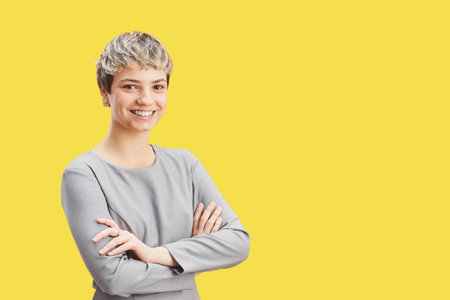 Waist up portrait of confident short-haired woman smiling at camera while standing with arms crossed...