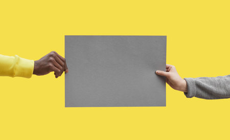 Graphic background image of two hands holding grey blank paper against pop yellow background, mock...