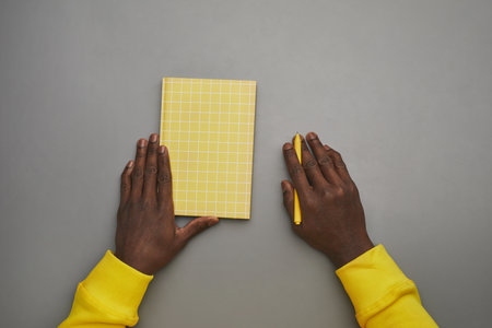 Minimal grey background of African-American male hands holding notebook or diary at desk, top down...