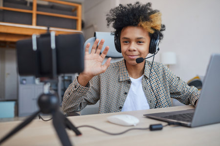 Portrait of teenage African-American boy wearing headset and waving at camera while streaming video games at home, young gamer or blogger concept, copy spaceの写真素材