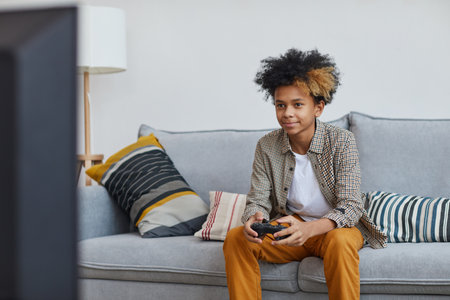 Minimal portrait of teenage African-American boy playing video games at home and smiling happily while holding gamepad, copy spaceの写真素材