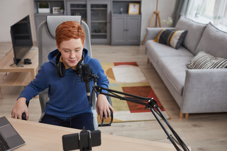 High angle portrait of red haired teenage boy speaking to microphone and recording video while streaming online, copy spaceの写真素材