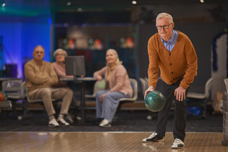 Full length portrait of active senior man playing bowling with group of friends in background, copy spaceの写真素材