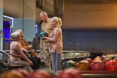 Wide angle side view at group of senior people playing bowling together while enjoying active entertainment at bowling alley, copy spaceの写真素材