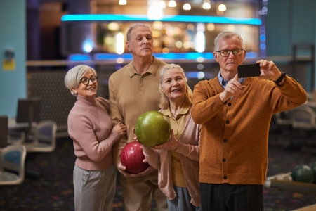 Group of senior people taking selfie photos playing bowling and enjoying active entertainment at bowling alleyの写真素材
