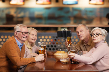 Group of modern senior people taking selfie photo while drinking beer in bowling bar and enjoying...