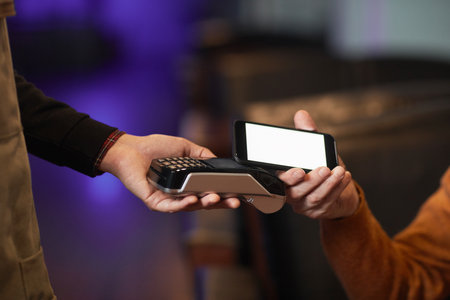 Side view close up of unrecognizable mature man paying via NFC with smartphone, focus on hand...