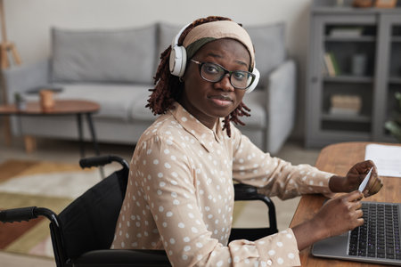 Portrait of African-American woman in wheelchair online shopping via laptop and looking at camera, copy spaceの写真素材