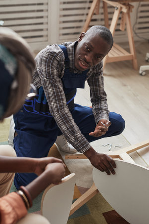 Vertical high angle portrait of African-American handyman helping young woman repair table and chairsの写真素材