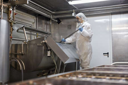 Wide angle portrait of young female worker mixing product at cheese and dairy factory, copy space