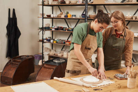 Warm toned portrait of two young people making ceramics while working at pottery workshop, small...