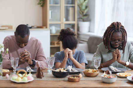 Portrait of modern African-American family saying grace at dinner table while celebrating easter at home, copy spaceの写真素材