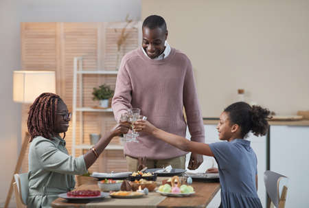 Portrait of modern African -American family clinking glasses and enjoying dinner together while celebrating Easter at home, copy spaceの写真素材