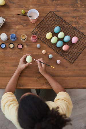 Vertical top view background of African-American girl painting pastel colored Easter eggs on wooden...