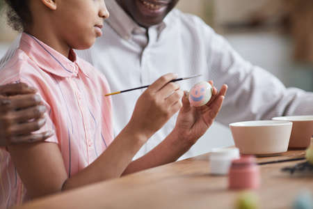 Cropped shot of young African-American girl painting pink Easter eggs while enjoying DIY decorating with father, copy spaceの写真素材