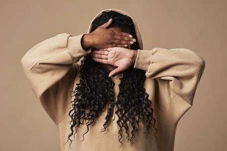 Minimal waist up portrait of young African American woman hiding face while posing against neutral beige background in studio, copy spaceの写真素材